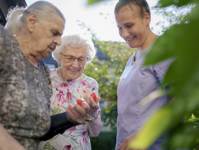 Zwei Seniorinnen im Theresianum im Sonnenschein mit Pflegerin beim Gärtnern