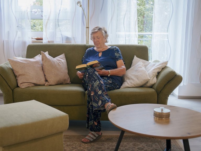 aeltere Frau sitzt auf einem Sofa und liest ein Buch