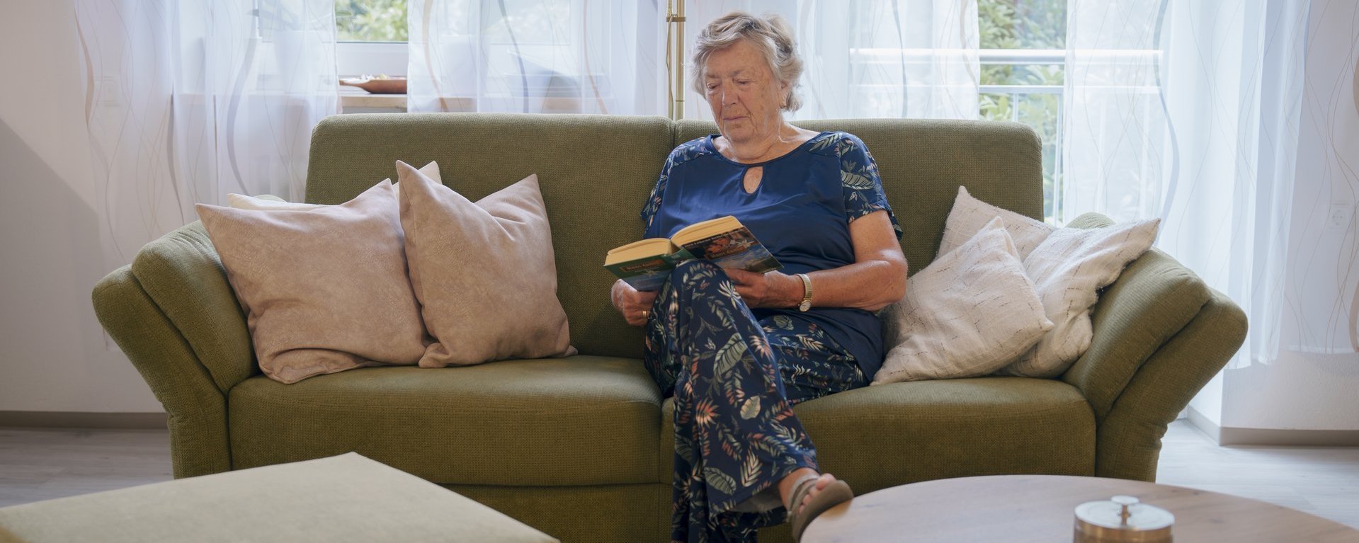 aeltere Frau sitzt auf einem Sofa und liest ein Buch