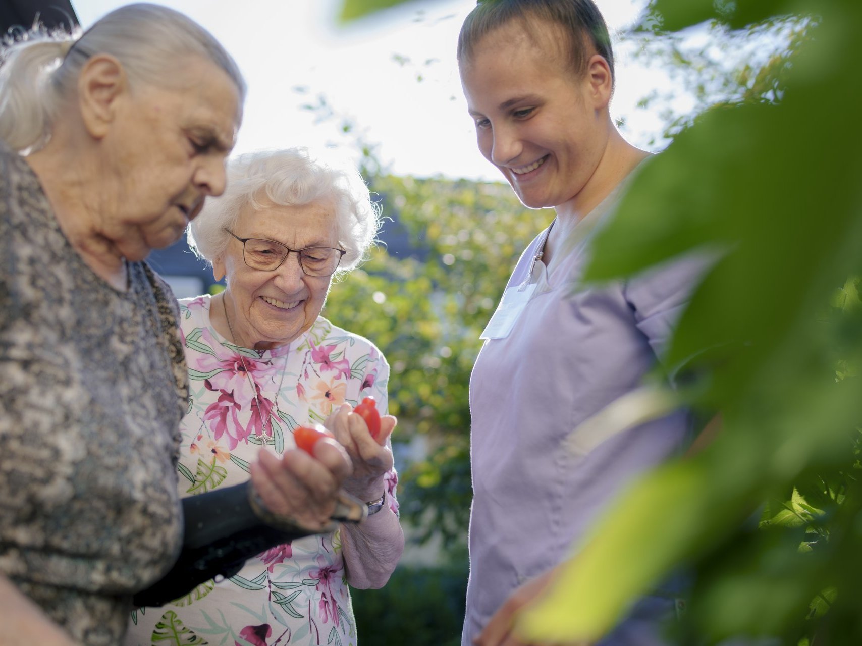 Zwei Seniorinnen und eine Pflegefachkraft arbeiten zufrieden im Garten